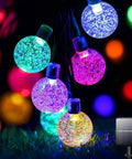 Solar Outdoor String Lights With 60 LED Crystal Globe Bulbs 8 Modes 26ft Waterproof Fairy Lights glowing on grass with solar panel