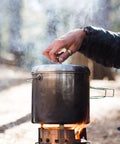 Pot 4000 Stainless Steel Camping Pot for outdoor cooking on campfire with foldable handles in use in forest setting.