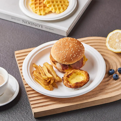 Heavy Duty 9 Inch Disposable Party Plates 150 Pack Eco Friendly Biodegradable Sugarcane Bagasse White Unbleached Dinner Plates For BBQs Picnics And Parties Compostable No Plastic holding a meal with burger, fries, and tart on a textured surface.