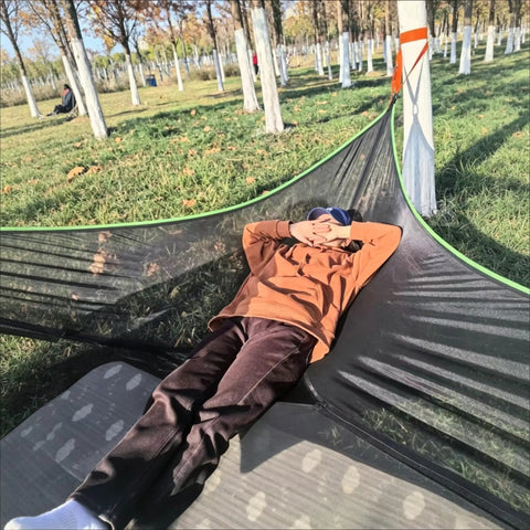 Person relaxing on Outdoor Triangular Hammock With Mesh Nylon, Portable 3 Point Design For Camping And Backyard Lounging.