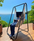 Weatherproof Hammock Chair Stand With Hanging Swing Chair Included, Rugged Iron Frame Supports Up To 450 Lbs on a patio by the sea