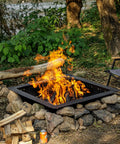 Heavy Duty 36 Inch Square Fire Pit Ring for DIY Campfire Inserts, surrounded by stones, in a natural setting with chairs.