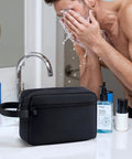 Travel Hanging Toiletry Bag With Carry Handle, water-resistant black bag on a bathroom counter with toiletries, compact size.
