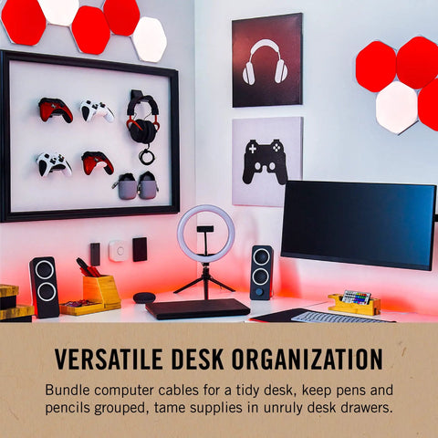 Modern desk setup with computer, speakers, gaming controllers, and red wall panels. "Versatile Desk Organization" sign visible.