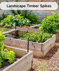 Raised garden beds with black stakes, labeled 'Landscape Timber Spikes', surrounded by greenery and brick wall.