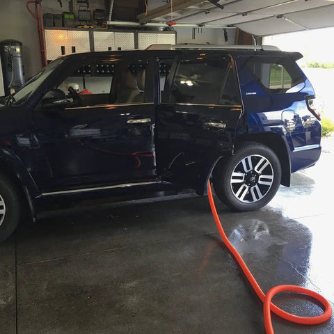 Central Vacuum Garage Attachment Kit With 50 Ft Hose cleaning car in garage, orange hose visible on wet floor