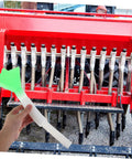 Hand holding the All In One Plastic Seed Tube Kit For Corn And Wheat Planters in front of a red seed drill machine.