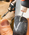 Carbide burr bits set with 1/8 in shanks for rotary tools; close-up of burr cutting metal jewelry and stone.