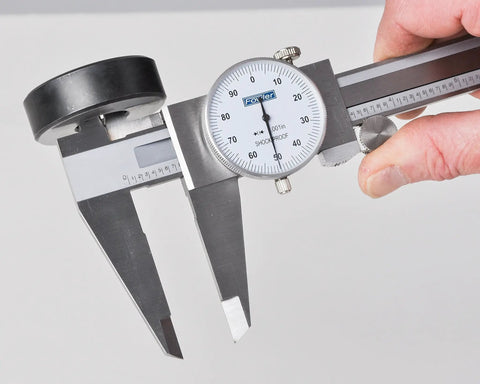 Hand holding dial caliper with 0-6 inch range, precision to 0.001 inch, measures inside, outside, depth and step, durable black body.
