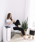 Woman relaxing next to PU4020 air purifier, uses Active Carbon Odor Filter For PU4020 Intense Pure Air Auto Purifier, kills bedroom odors.