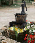 27 Inch Tall Outdoor Barrel Water Fountain With Two Tier Cascading Waterfall And Electric Recirculating Pump Bronze Garden Decor For Patio Yard Porch Or Landscape Creates Soothing Sound And Relaxing Outdoor Vibe, surrounded by flowers