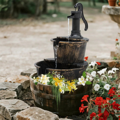 27 Inch Tall Outdoor Barrel Water Fountain With Two Tier Cascading Waterfall And Electric Recirculating Pump Bronze Garden Decor For Patio Yard Porch Or Landscape Creates Soothing Sound And Relaxing Outdoor Vibe, surrounded by flowers