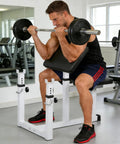 Man using adjustable preacher curl bench with barbell rack for home gym, seated strength training station, steel construction