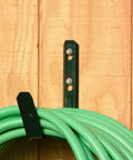 Green hose coil on black metal wall bracket against wooden background