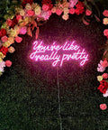 Pink 'You Are Like Really Pretty Neon Lights Sign for Wall Decor Bar Salon Home Shop and Party Large Dimmable Pink Neon LED Sign Perfect for Wedding and Birthday Vibe and Insta Ready Rooms' on floral wall.