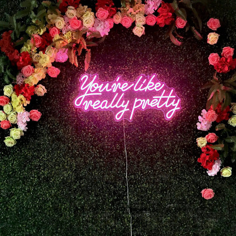Pink 'You Are Like Really Pretty Neon Lights Sign for Wall Decor Bar Salon Home Shop and Party Large Dimmable Pink Neon LED Sign Perfect for Wedding and Birthday Vibe and Insta Ready Rooms' on floral wall.