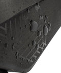 Close-up of the waterproof surface of the Midloader Drybag For Bike Frame Waterproof Medium Size With Hidden Weatherproof Zipper And Flap Reflective Logo Dual Side Zippers And Slim Pocket For Small Gear TPU Construction For Commuters And Trail Riders Go To Everyday Rides showcasing water droplets on black material with reflective logo.