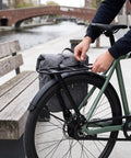 Sleek Carbon Fiber And Aluminum Rear Bike Rack For Mountain And Road Bikes Built Different To Haul Gear Reliably Every Time Without Extra Bulk Or Concerns, shown attaching to bike with commuter bag.