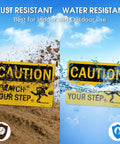 Kickass Caution Watch Your Step Signs 2 Pack 10 X 7 Inch Rust Free Reflective Aluminum Safety Plaque shown in dirt and water.
