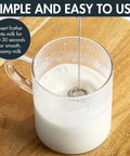 Handheld frother in glass cup of milk, demonstrating use with Compact Stovetop Espresso Maker And Handheld Electric Milk Frother Gift Set Pro Grade Aluminum Moka Pot For Rich Italian Cuban Coffee Six Sleek Demitasse Cups For Next Level Daily Grind Sips.