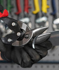 Close-up of left-cut offset aviation snips (tin snips) with dark metal blades and red handle, held by gloved hand.