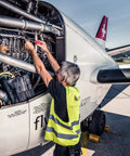 Mechanic using SwissGrip Slotted And Phillips Screwdriver Kit on aircraft engine, wearing safety vest, outdoor airfield setting.