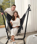 Couple enjoying Cozy Macrame Hammock With Stand And Phone Holder, Double Hanging Swing Chair in living room, natural light.