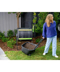 Woman using Dual Chamber 48 Gallon Compost Tumbler With Geared Rotation And Cart Access For Easy Turning Of Kitchen Scraps And Yard Waste