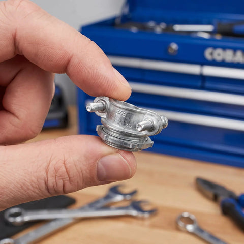 Hand holding a zinc alloy cable clamp, showcasing threaded connectors for electrical conduit wiring. Heavy Duty Four Pack Three Quarter Inch Cable Clamps Zinc Alloy Threaded Connectors For Electrical Conduit Wiring With Knockout Vibration Resistance And No Fuss Mounting Built Badass Tough.