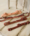 Assorted All American Tack Button Bit Hobble made from premium one half inch Latigo leather, built in the USA, on wooden surface.