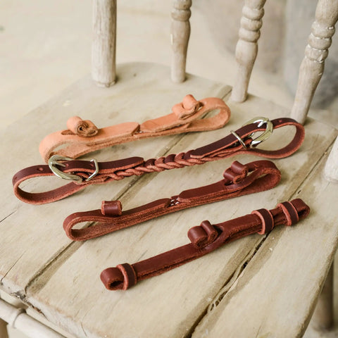 Assorted All American Tack Button Bit Hobble made from premium one half inch Latigo leather, built in the USA, on wooden surface.