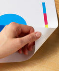 Hand holding corner of colorful printed paper on wood surface showing vibrant design, using Real Deal Multipurpose Copy Printer Paper 8 Ream Case 4000 Sheets 20 Lb Letter Size 8.5 X 11 Inches 92 Bright White.