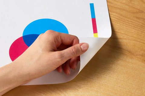 Hand holding corner of colorful printed paper on wood surface showing vibrant design, using Real Deal Multipurpose Copy Printer Paper 8 Ream Case 4000 Sheets 20 Lb Letter Size 8.5 X 11 Inches 92 Bright White.