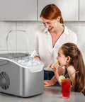 Portable Countertop Ice Maker With Handle Delivers 9 Bullet Shaped Ice Cubes In About 6 Minutes 26 Lbs Per Day Self Cleaning Function Includes Ice Scoop And Basket For Home Kitchen Party Ready Grey in use by woman and child on kitchen countertop.