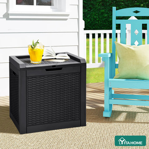32 Gallon Outdoor Storage Box With Lockable Lid And Side Handles, Waterproof Resin Rattan Deck Box For Patio Cushions, Tools, Pool Accessories, And More, Versatile Side Table Or Storage Ottoman, Black next to a patio chair with a drink on top.