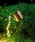 Sun Powered Watering Can Lights For Garden With Cascading LED Pouring Water Effect illuminated among garden foliage at night