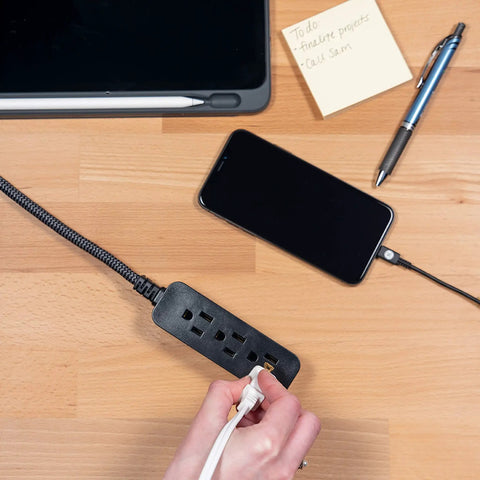 Pro Mini 3 Outlet Power Strip With 6 Inch Designer Braided Cord, in use on a desk with phone charging, flat plug visible.