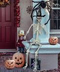 5.4Ft Life Size Halloween Skeleton With Movable Joints sitting on a porch with pumpkins, wearing a witch hat