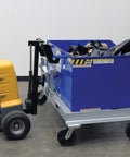 Heavy Duty Electric Powered Tugger With 1000 Lb Pull Capacity For Effortless Factory Material Handling Featuring Ergonomic Handle And Dead Man Switch Safety System In Bright Yellow Black Finish next to blue container.