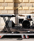 Outdoor music setup with a keyboard on a stand, drum set, and amplifier on a mobile stage with caster wheels visible.