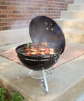 Smokey Joe 14 Inch Portable Charcoal Grill with Tuck N Carry Lid open, outdoor cooking on patio, holding skewers.
