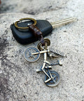 Vintage Leather And Bronze Bicycle Keychain With Metal Wheel And Handlebars Pendant, shown with car key on stone surface.