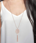 Woman wearing long layered necklace set with oval disk pendant and tassel fringe Y shape in rose gold for everyday or party