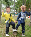 Two children wearing lightweight water bottle holders with adjustable straps for walking and hiking in a park setting.