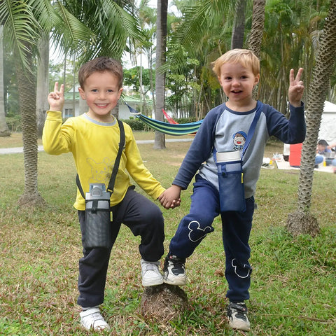 Two children wearing lightweight water bottle holders with adjustable straps for walking and hiking in a park setting.