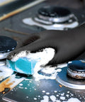 Hella Durable Black Nitrile Safety Gloves With Sick PyraGrip Texture For Superior Traction On Greasy Jobs Heavy Duty Industrial Gear in use while cleaning a stove.