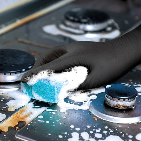 Hella Durable Black Nitrile Safety Gloves With Sick PyraGrip Texture For Superior Traction On Greasy Jobs Heavy Duty Industrial Gear in use while cleaning a stove.