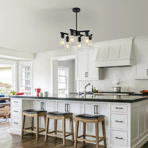 Six Light Matte Black Modern Farmhouse Chandelier With Clear Glass Shades hanging above kitchen island with stools.