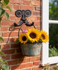 Badass Vintage Cast Iron Beard Shaped Wall Hook Kit holding a bucket of sunflowers on a brick wall for home decor.