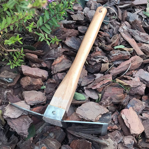 Heavy Duty Stainless Steel Pickaxe Hoe With Wooden Handle for Digging in the Garden resting on mulch